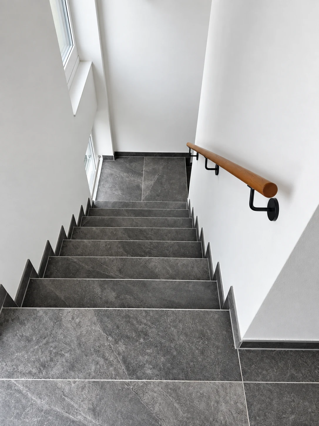 Treppe mit grauem Fliesenbelag und Holzhandlauf