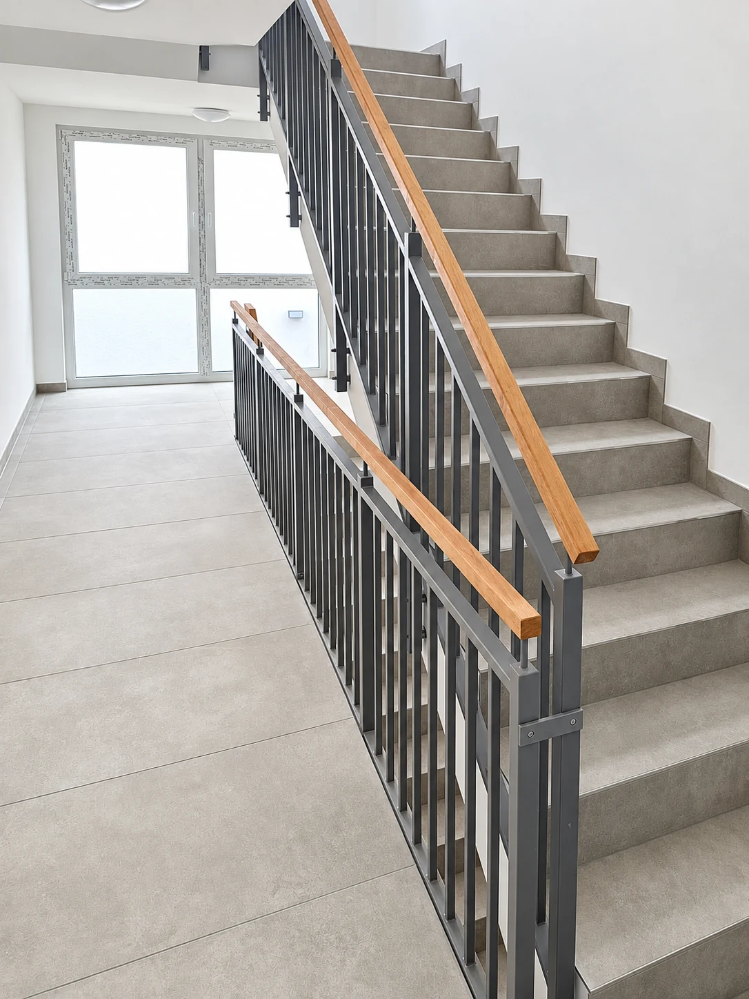 Gefliestes Treppenhaus mit Metallgeländer und Holzhandlauf